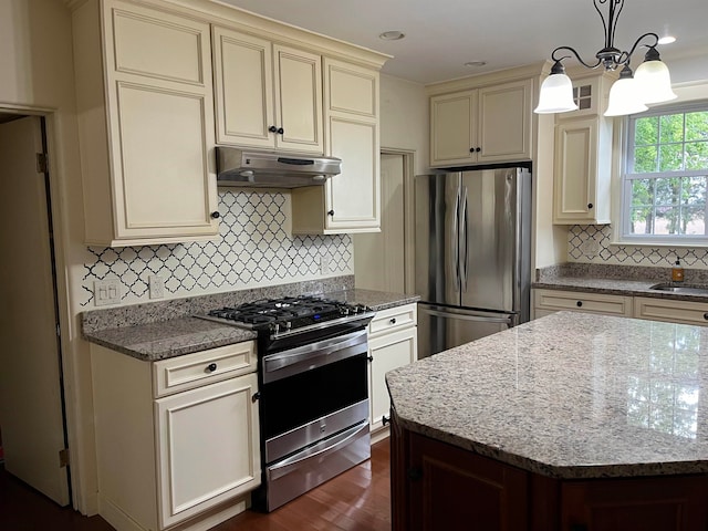 kitchen featuring decorative light fixtures, light stone countertops, stainless steel appliances, and cream cabinets