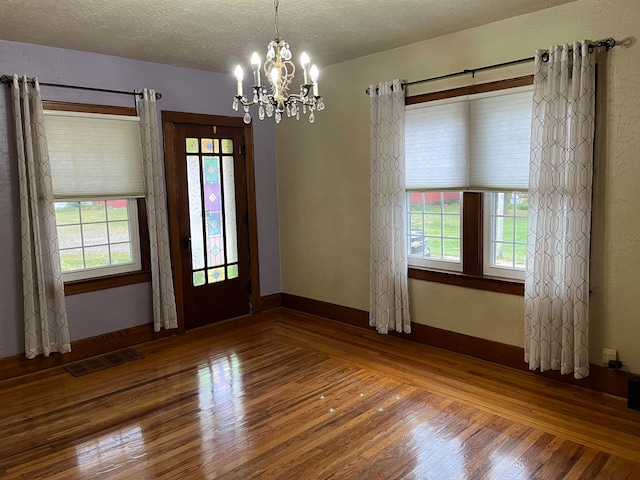 spare room featuring wood-type flooring, a textured ceiling, a wealth of natural light, and a chandelier