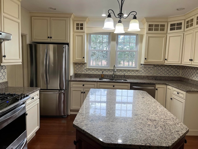 kitchen with appliances with stainless steel finishes, sink, cream cabinets, decorative light fixtures, and a kitchen island