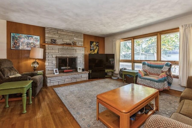 living room featuring a textured ceiling, a stone fireplace, dark wood-type flooring, and wood walls