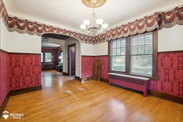 unfurnished dining area featuring hardwood / wood-style flooring, a notable chandelier, and radiator