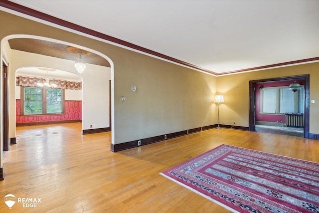 unfurnished room with hardwood / wood-style flooring, an inviting chandelier, radiator, and ornamental molding