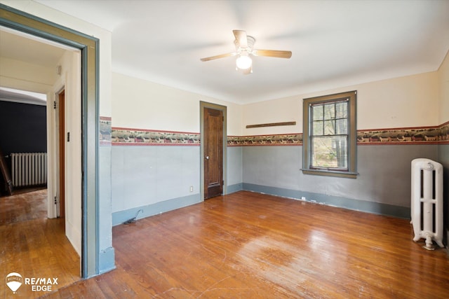 empty room with hardwood / wood-style flooring, ceiling fan, and radiator