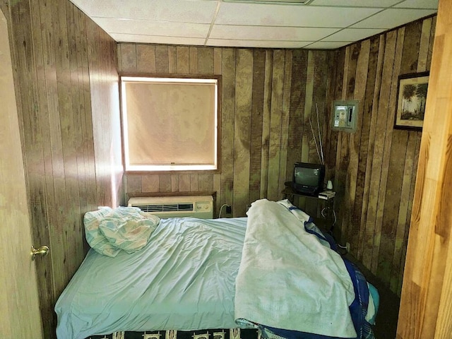 bedroom with a wall unit AC, a paneled ceiling, and wooden walls