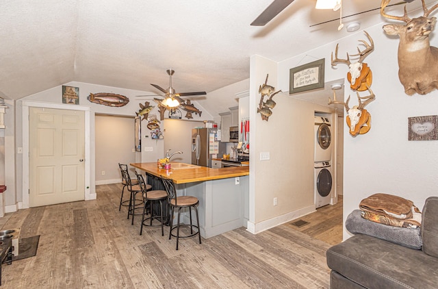 kitchen featuring a kitchen bar, stainless steel appliances, vaulted ceiling, stacked washer / dryer, and butcher block countertops