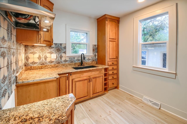 kitchen featuring tasteful backsplash, light stone countertops, sink, and light hardwood / wood-style floors