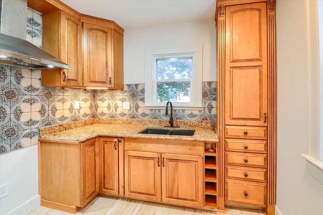 kitchen featuring light stone countertops, sink, wall chimney range hood, decorative backsplash, and light wood-type flooring