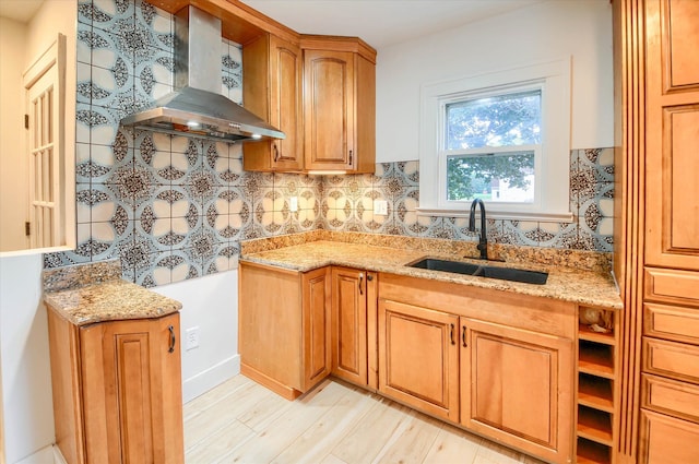 kitchen featuring light stone countertops, light wood-type flooring, backsplash, wall chimney exhaust hood, and sink