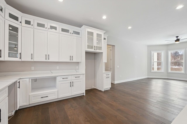 kitchen with light stone countertops, dark hardwood / wood-style floors, white cabinets, and ceiling fan