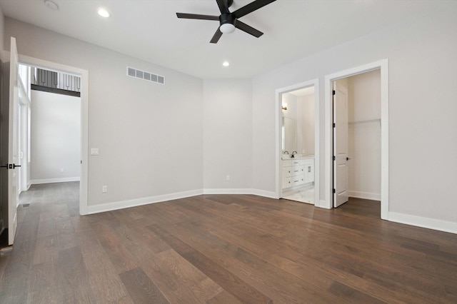 unfurnished bedroom featuring ensuite bathroom, dark wood-type flooring, ceiling fan, and a spacious closet