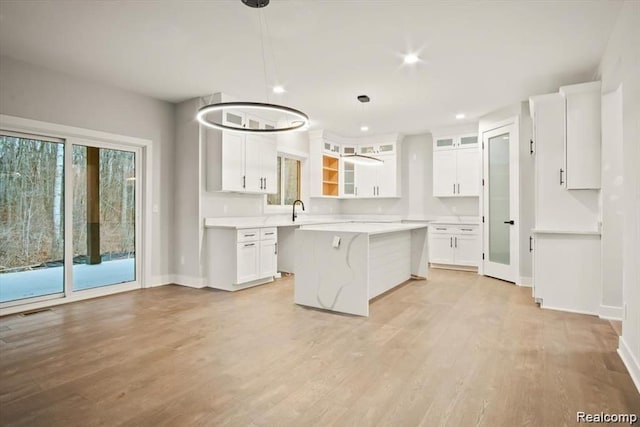 kitchen with white cabinets, pendant lighting, a center island, and light hardwood / wood-style floors