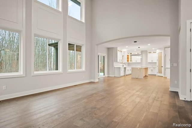 unfurnished living room featuring hardwood / wood-style floors, a towering ceiling, plenty of natural light, and sink