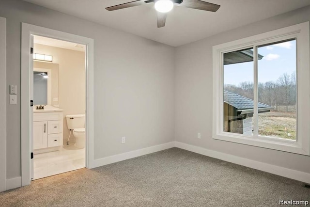 unfurnished bedroom featuring ensuite bath, ceiling fan, carpet floors, and multiple windows