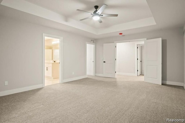 unfurnished bedroom featuring a tray ceiling, ensuite bathroom, ceiling fan, and light colored carpet