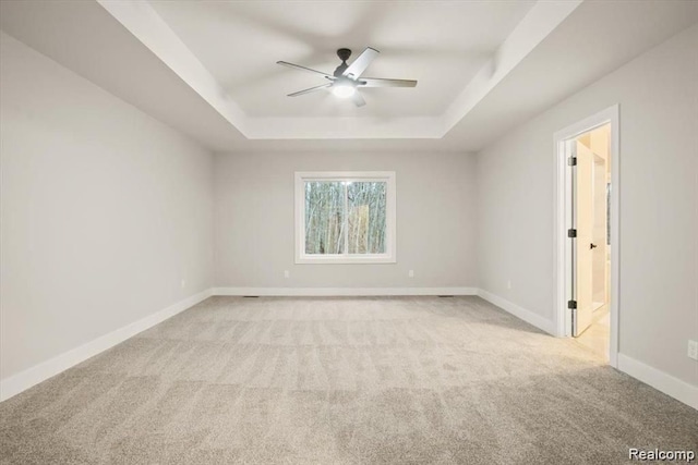 carpeted empty room with a raised ceiling and ceiling fan