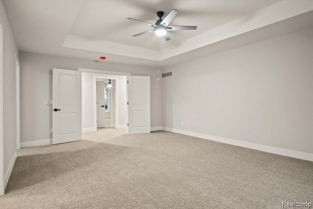 unfurnished bedroom with a tray ceiling, ceiling fan, and light carpet