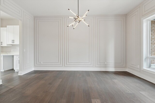 unfurnished dining area with a decorative wall, dark wood-style flooring, and a notable chandelier