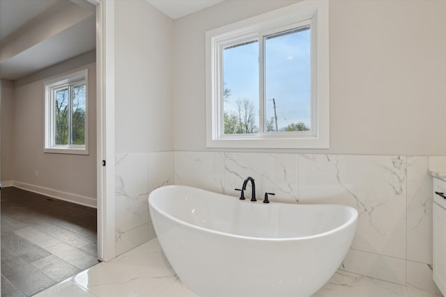 full bathroom with a freestanding tub, tile walls, a wainscoted wall, and marble finish floor