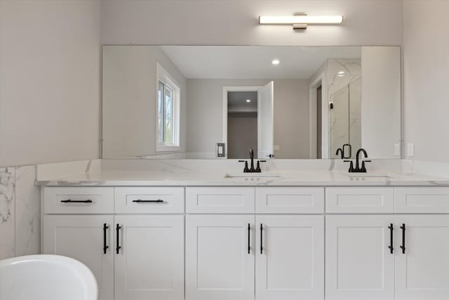bathroom featuring a sink, a marble finish shower, and double vanity