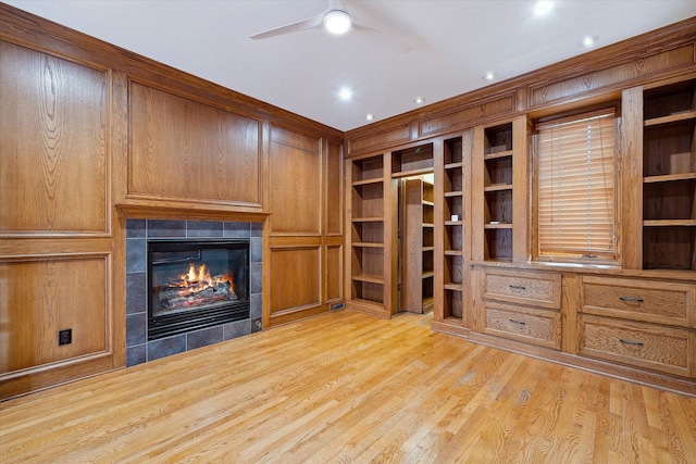 unfurnished living room featuring ceiling fan, built in features, a tile fireplace, and light hardwood / wood-style flooring