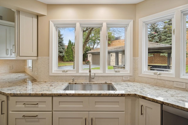 kitchen featuring decorative backsplash, light stone counters, sink, and white cabinets