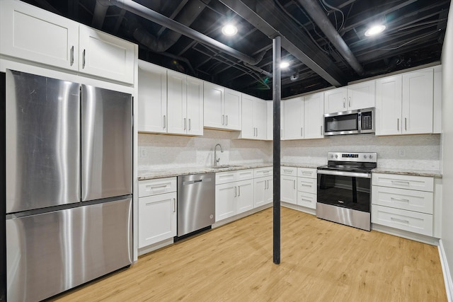 kitchen with sink, light hardwood / wood-style flooring, appliances with stainless steel finishes, light stone counters, and white cabinetry