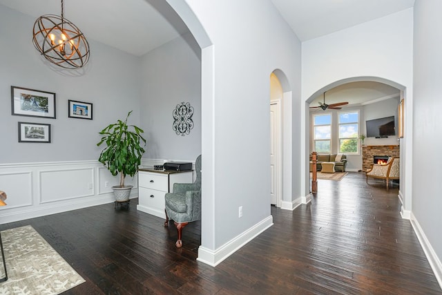 interior space featuring a stone fireplace, ceiling fan with notable chandelier, and dark hardwood / wood-style floors