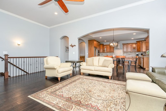 living room with dark hardwood / wood-style flooring, crown molding, and ceiling fan with notable chandelier