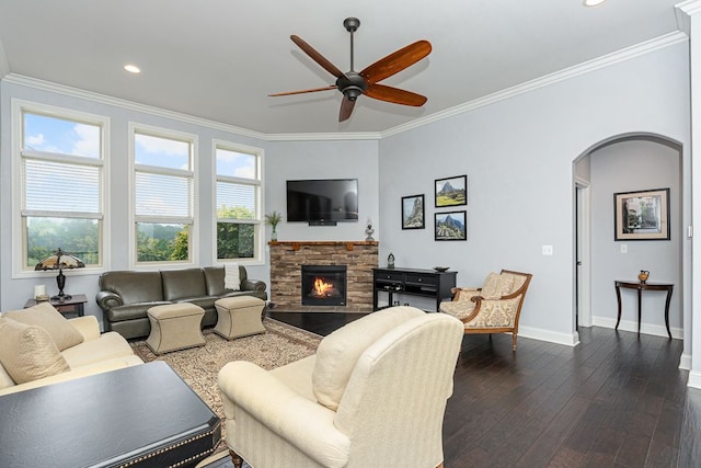 living room with crown molding, a stone fireplace, dark hardwood / wood-style floors, and ceiling fan