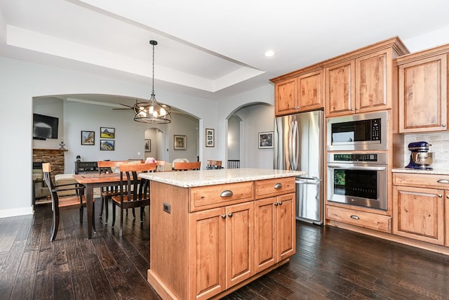 kitchen with a kitchen island, appliances with stainless steel finishes, pendant lighting, a raised ceiling, and dark wood-type flooring