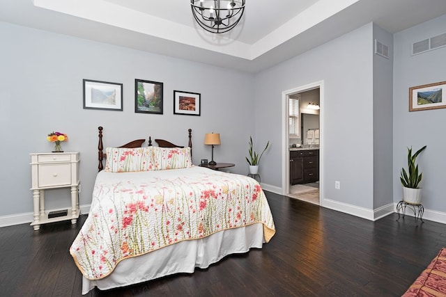 bedroom featuring a raised ceiling, dark hardwood / wood-style floors, connected bathroom, and a chandelier