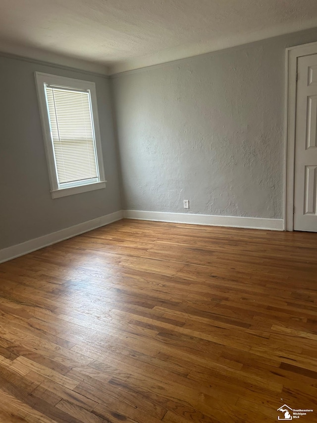 unfurnished room featuring a textured wall, wood finished floors, and baseboards