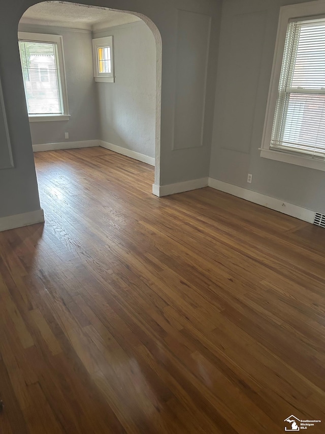 empty room featuring arched walkways, dark wood-style flooring, visible vents, and baseboards