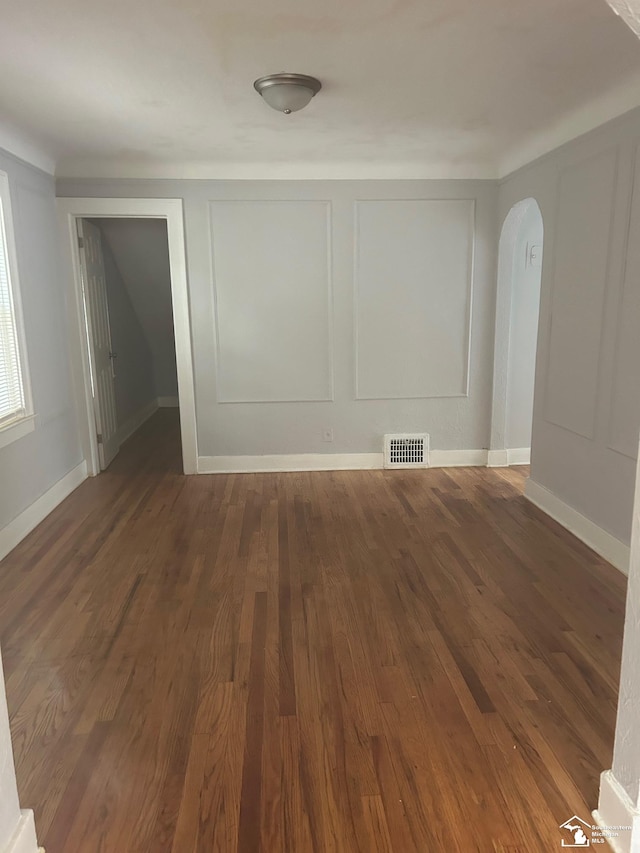 empty room featuring arched walkways, visible vents, a decorative wall, and dark wood finished floors