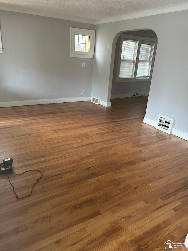 empty room with arched walkways, dark wood-style flooring, and visible vents