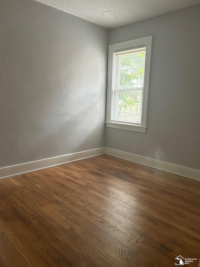 empty room with dark wood-type flooring, a textured ceiling, and baseboards