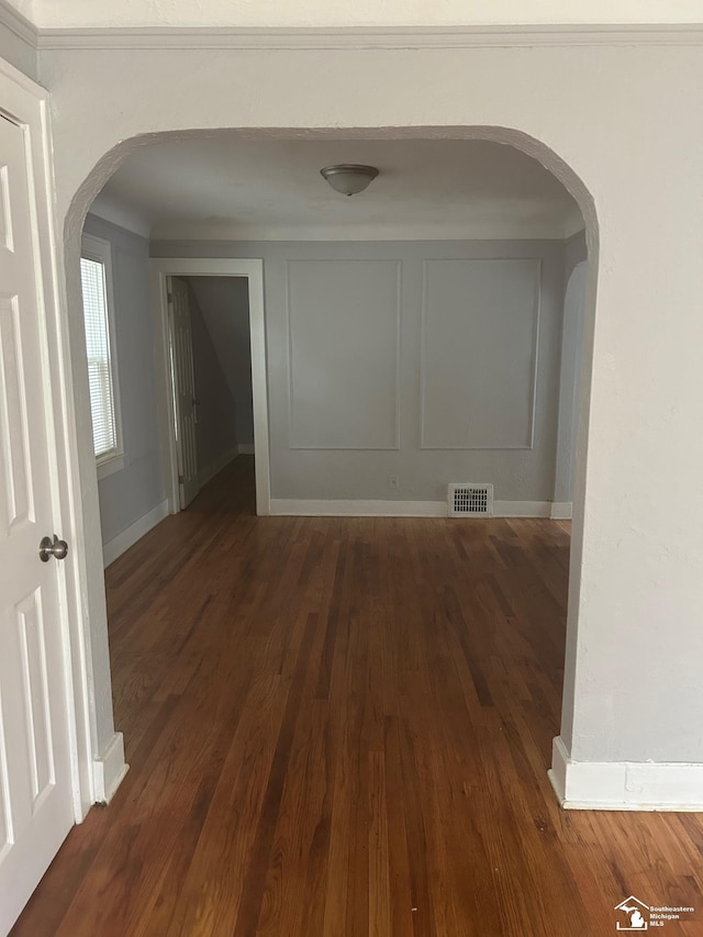 corridor with baseboards, visible vents, arched walkways, and dark wood-style flooring