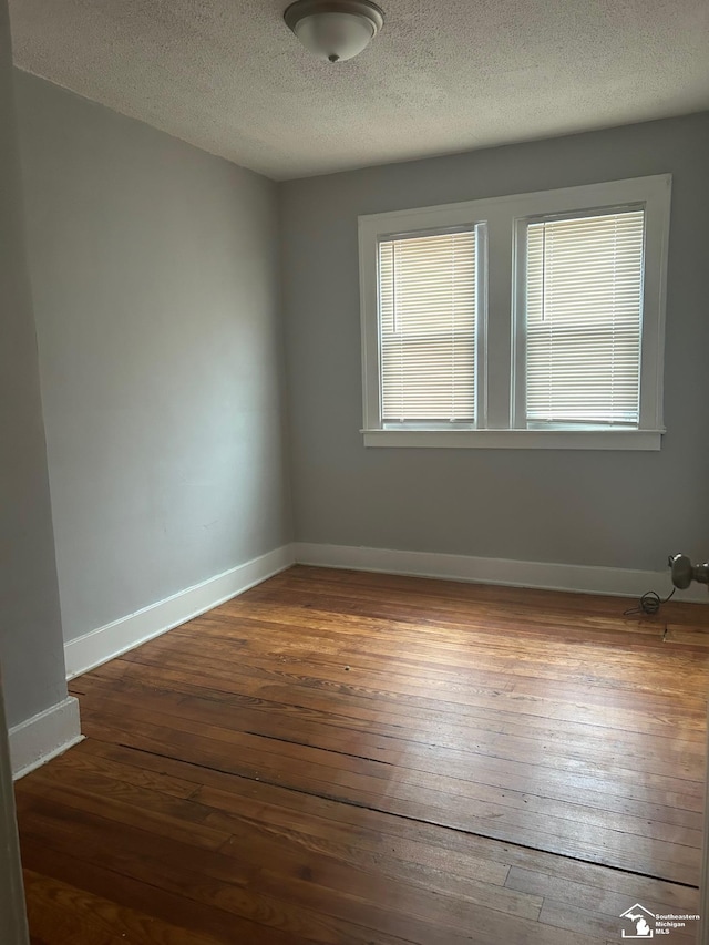 unfurnished room with dark wood-type flooring, a textured ceiling, and baseboards