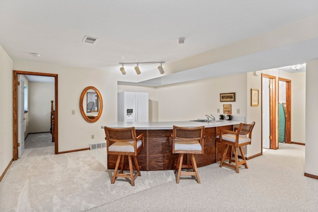 bar featuring light carpet, track lighting, and white fridge with ice dispenser