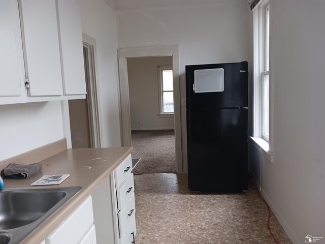 kitchen with carpet, black fridge, white cabinetry, and sink