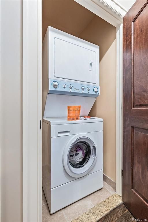 clothes washing area with light tile patterned floors and stacked washing maching and dryer