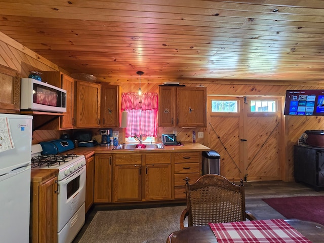 kitchen with sink, white appliances, hanging light fixtures, and wooden walls