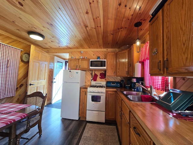 kitchen featuring dark hardwood / wood-style flooring, white appliances, sink, hanging light fixtures, and wood walls