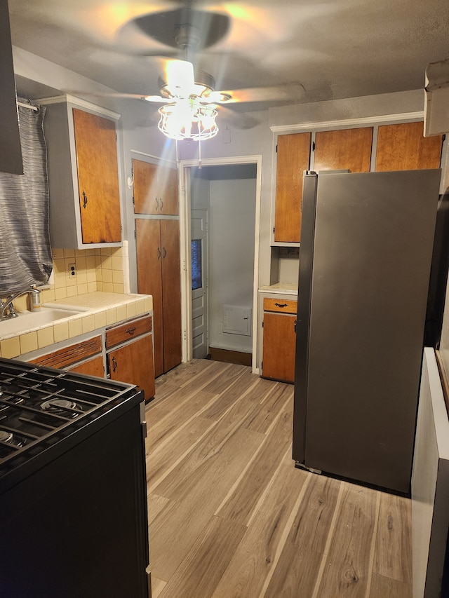 kitchen with stainless steel refrigerator, tasteful backsplash, stove, tile counters, and light hardwood / wood-style flooring