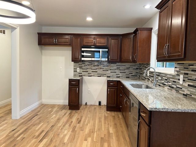 kitchen with appliances with stainless steel finishes, tasteful backsplash, light hardwood / wood-style flooring, and light stone counters