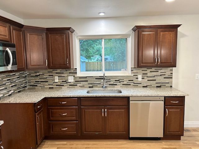 kitchen with decorative backsplash, light wood-type flooring, light stone counters, stainless steel appliances, and sink