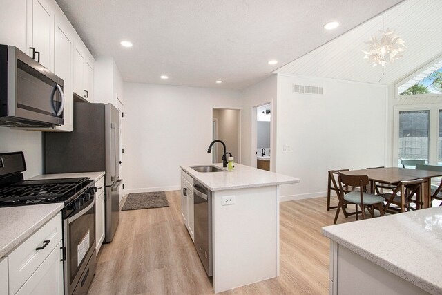 kitchen featuring sink, white cabinets, hanging light fixtures, stainless steel appliances, and a center island with sink