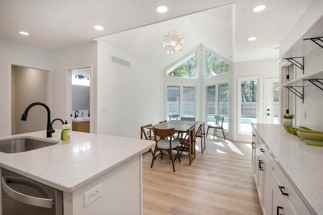 kitchen featuring sink, light hardwood / wood-style floors, white cabinets, a center island with sink, and vaulted ceiling