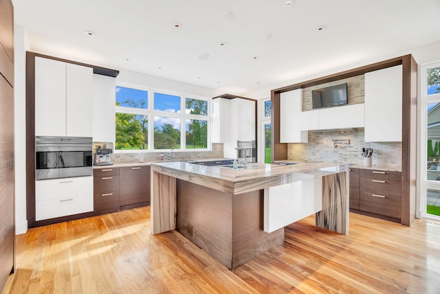 kitchen with stainless steel oven, light hardwood / wood-style flooring, dark brown cabinets, light stone counters, and white cabinetry