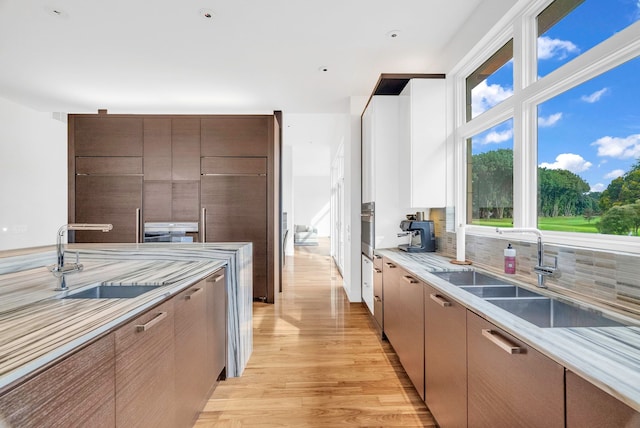 kitchen with decorative backsplash, sink, oven, and light hardwood / wood-style flooring